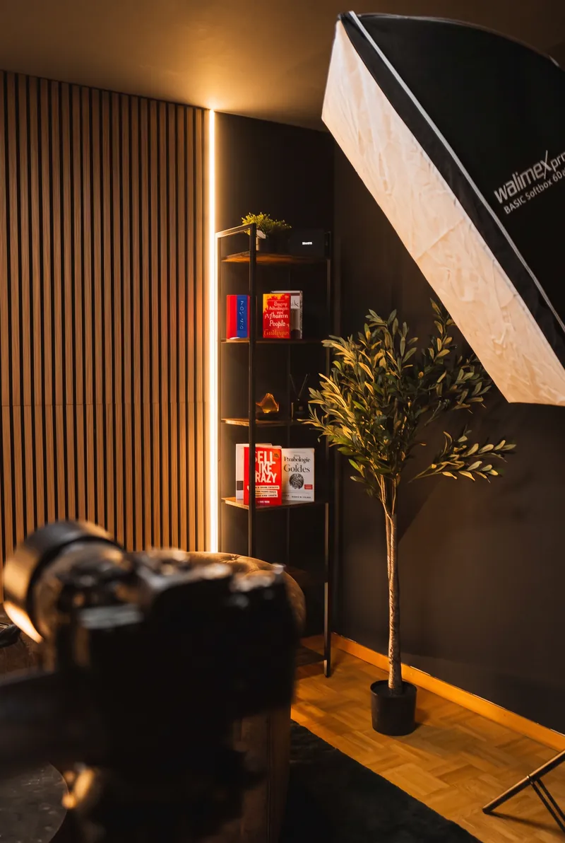 Hochformat-Detail: Kamera im Vordergrund, dahinter Softbox, Bücherregal und Olivenbaum