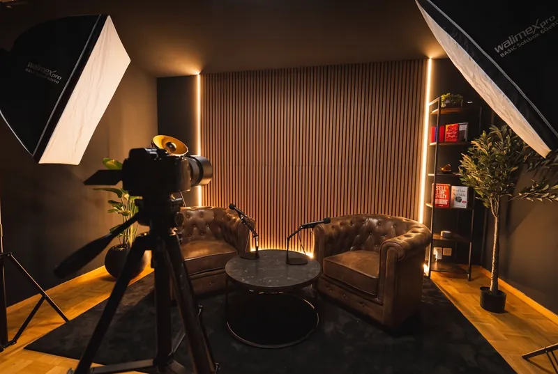 Das ganze Set im Weitwinkel: Kamera auf dem Stativ, zwei Softboxen, Sessel und Tisch vor der Holzlamellenwand