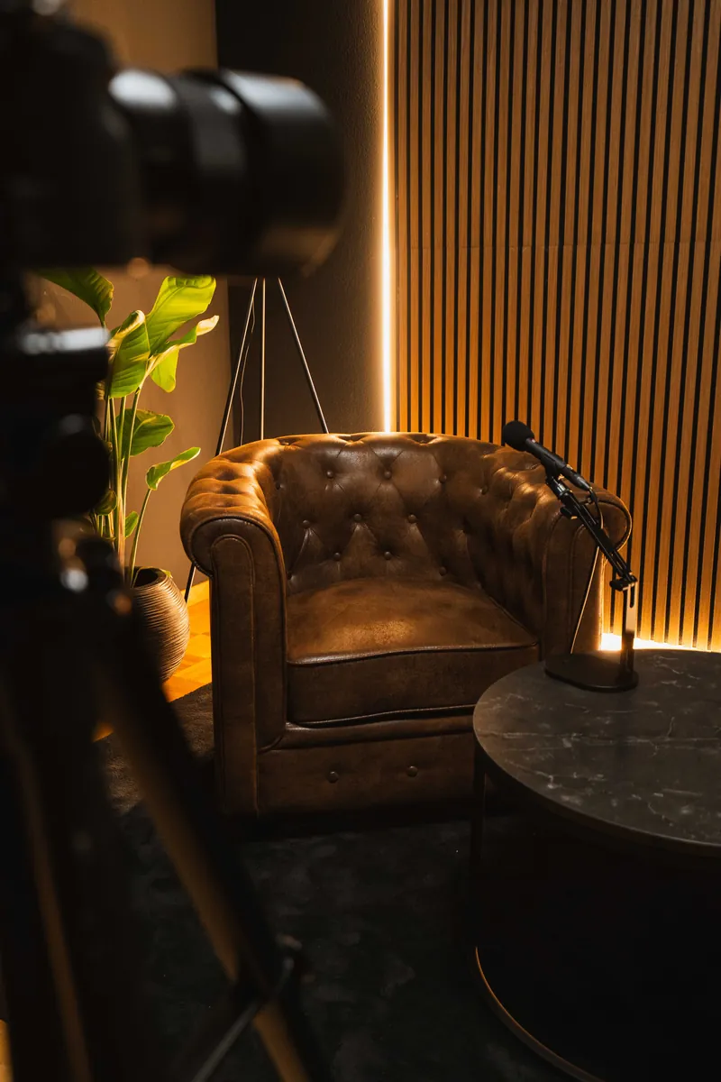 Blick an der Kamera vorbei auf einen Chesterfield-Sessel, das Mikrofon und den runden Tisch